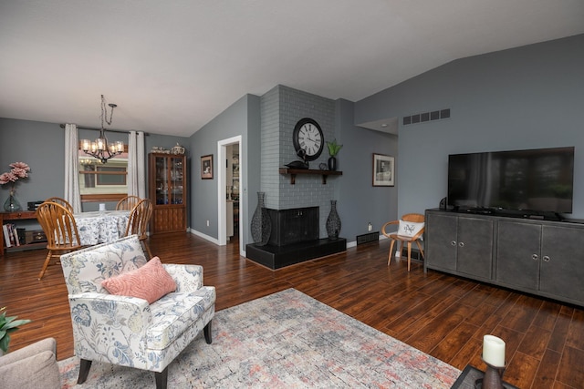 living area with vaulted ceiling, a chandelier, wood finished floors, a brick fireplace, and baseboards