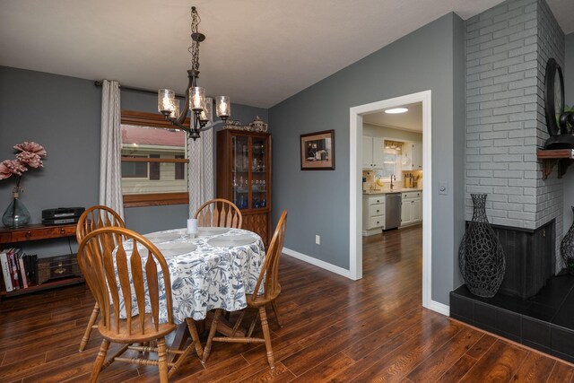 dining room with a chandelier, vaulted ceiling, dark wood finished floors, baseboards, and a brick fireplace