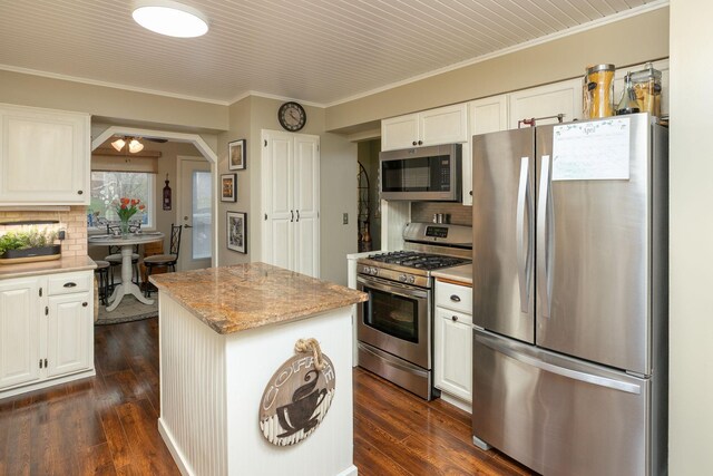 kitchen featuring appliances with stainless steel finishes, a center island, tasteful backsplash, a ceiling fan, and ornamental molding