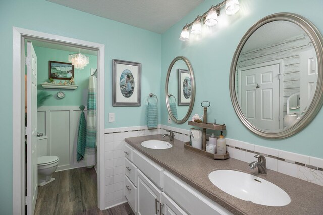 bathroom featuring wainscoting, wood finished floors, double vanity, toilet, and a chandelier