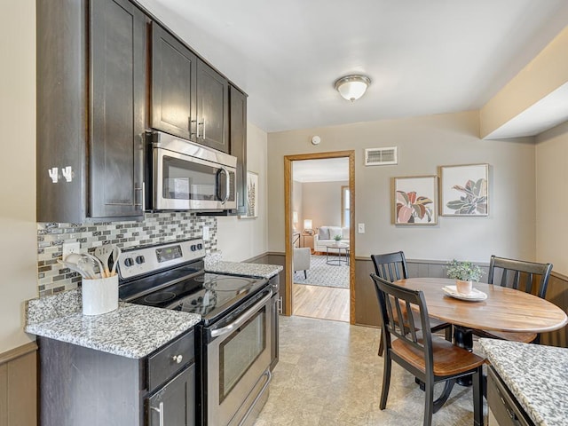 kitchen featuring appliances with stainless steel finishes, decorative backsplash, light stone counters, light floors, and dark brown cabinets