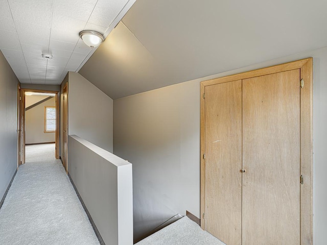 hallway featuring an upstairs landing, light carpet, baseboards, and lofted ceiling