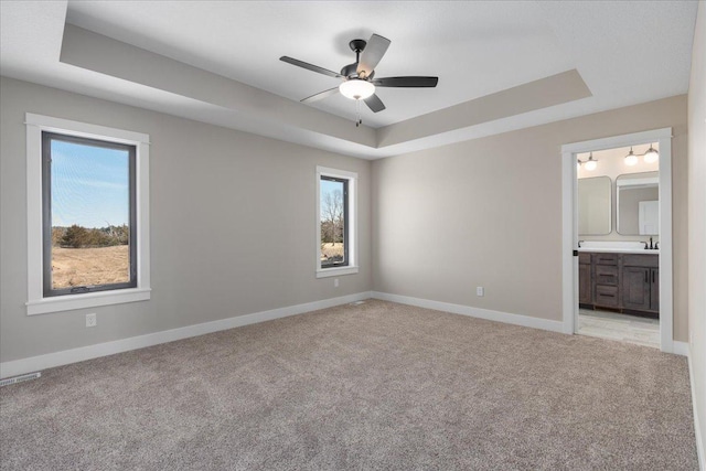 unfurnished bedroom with a raised ceiling, visible vents, baseboards, and light colored carpet