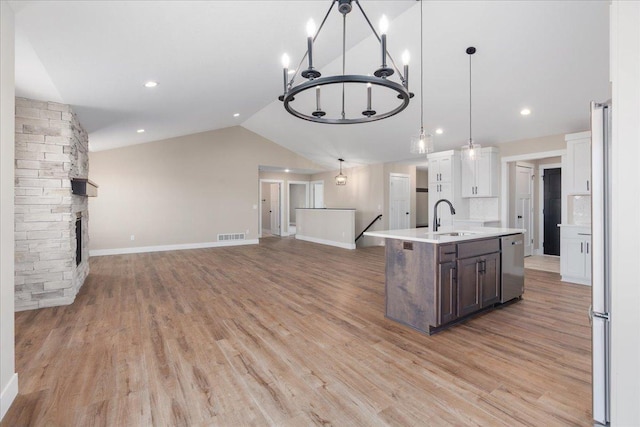 kitchen with a sink, light countertops, open floor plan, stainless steel dishwasher, and a center island with sink