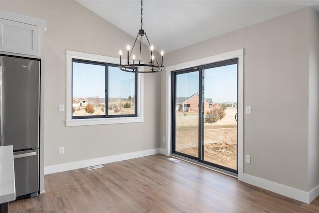 unfurnished dining area featuring a chandelier, visible vents, wood finished floors, baseboards, and lofted ceiling