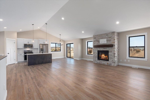 unfurnished living room featuring a stone fireplace, light wood-type flooring, baseboards, high vaulted ceiling, and a chandelier