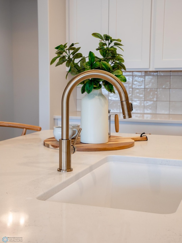 room details featuring white cabinets, light stone counters, and a sink