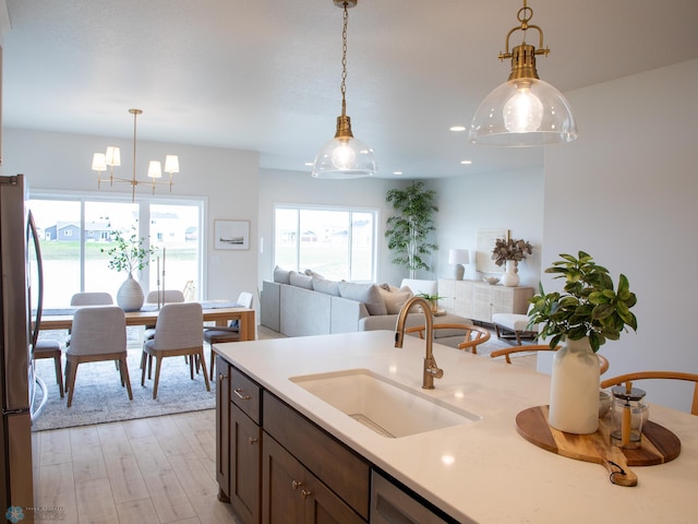 kitchen with freestanding refrigerator, light wood-type flooring, light countertops, a sink, and hanging light fixtures