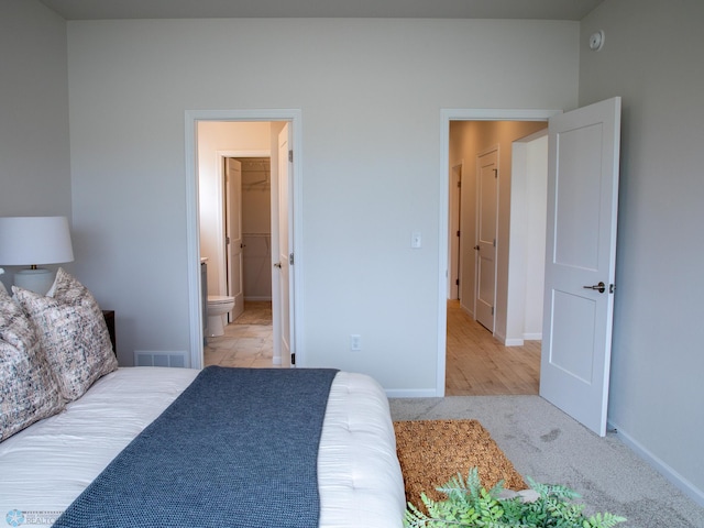 bedroom with visible vents, baseboards, ensuite bath, and light carpet