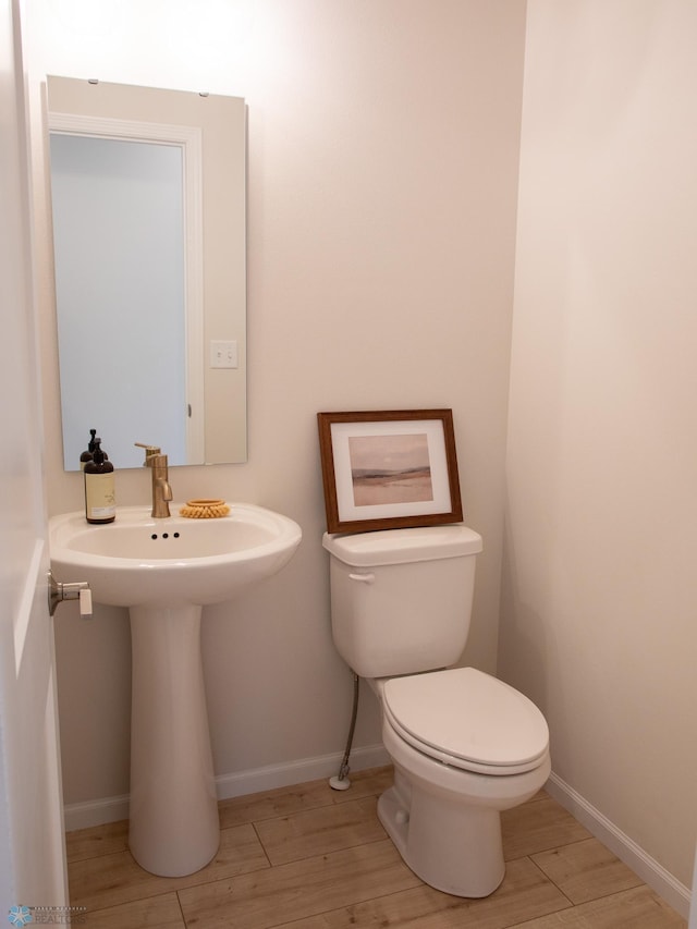 half bath featuring a sink, baseboards, toilet, and wood finished floors