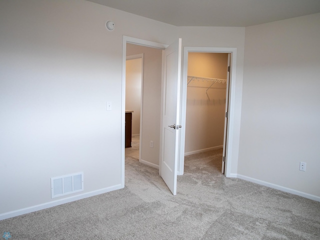 unfurnished bedroom featuring a walk in closet, visible vents, baseboards, a closet, and carpet flooring