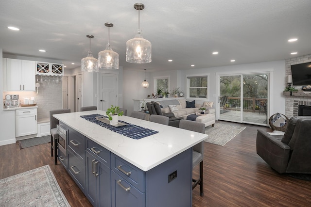 kitchen featuring a breakfast bar, open floor plan, a center island, white cabinets, and dark wood finished floors
