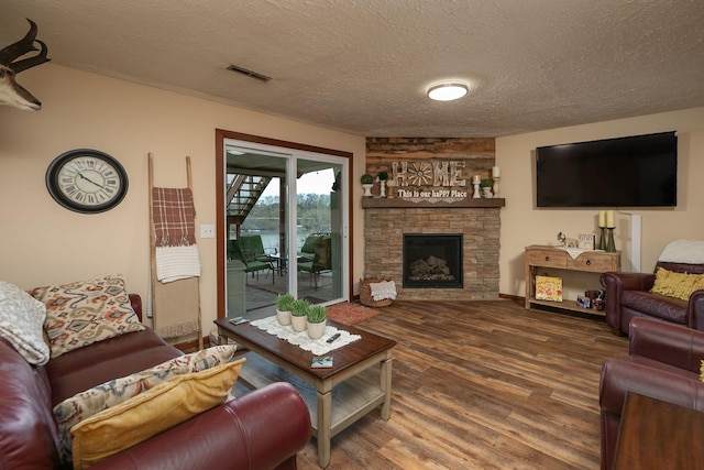 living room featuring a textured ceiling, a fireplace, wood finished floors, and visible vents