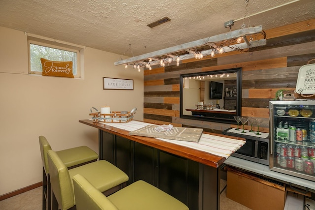 bar featuring visible vents, wood walls, a textured ceiling, and stainless steel microwave