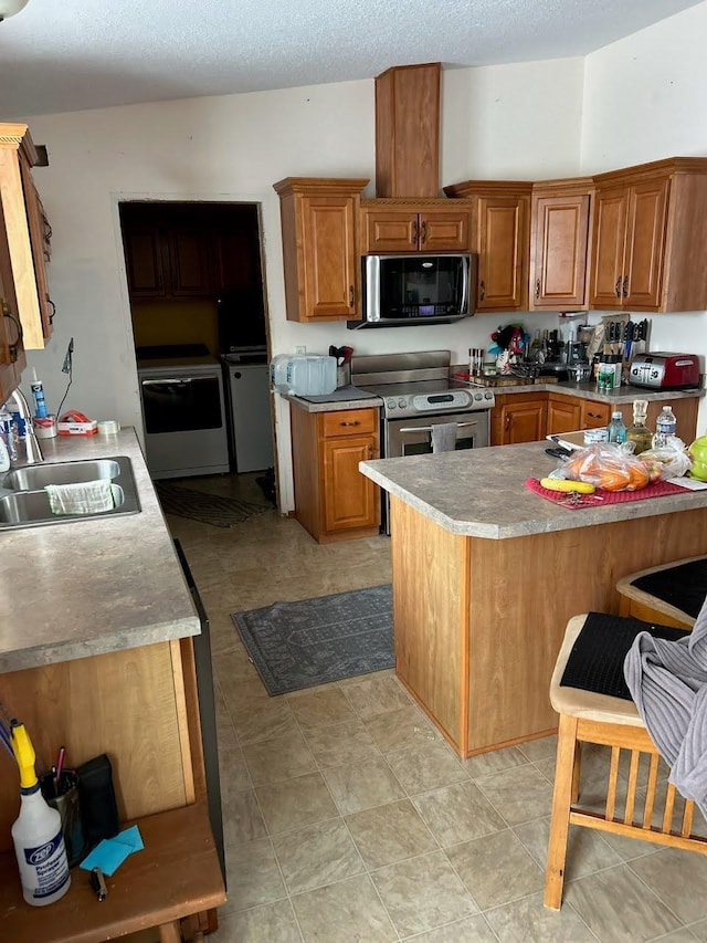 kitchen with brown cabinetry, a sink, a peninsula, stainless steel appliances, and washer and clothes dryer