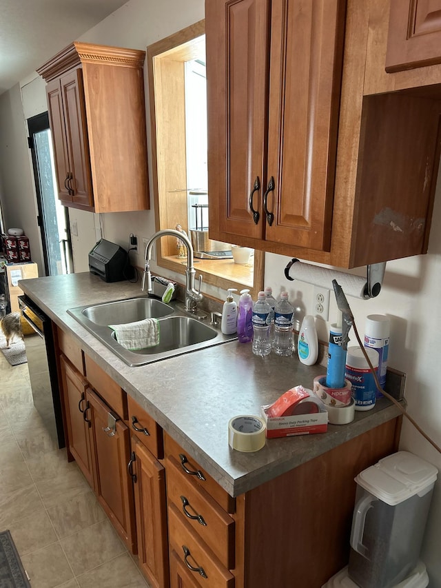 kitchen featuring stainless steel dishwasher, light tile patterned flooring, brown cabinetry, and a sink