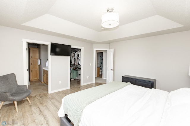bedroom featuring a walk in closet, a raised ceiling, a closet, light wood-style floors, and ensuite bathroom