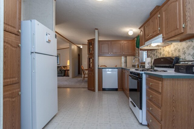 kitchen with a sink, white appliances, a textured ceiling, light floors, and under cabinet range hood