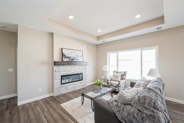 living area featuring wood finished floors, a fireplace, baseboards, recessed lighting, and a raised ceiling