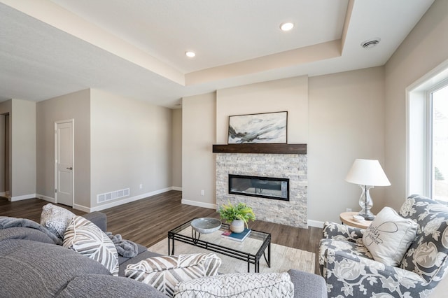 living room featuring visible vents, baseboards, wood finished floors, and a stone fireplace