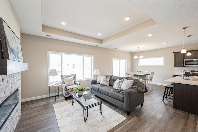living area featuring a stone fireplace, baseboards, dark wood finished floors, and a healthy amount of sunlight