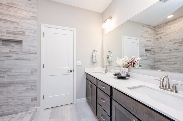 full bathroom featuring double vanity, a sink, baseboards, and tiled shower