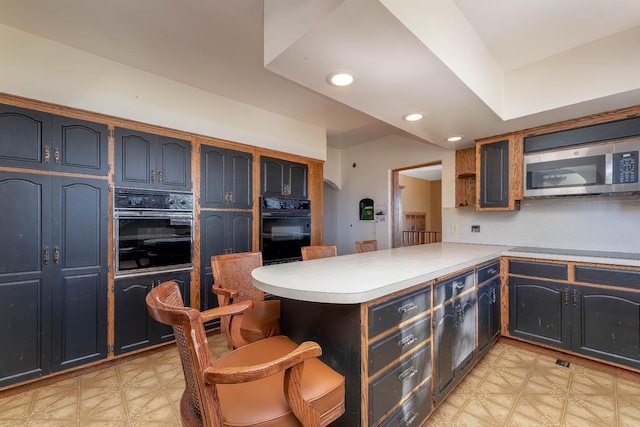 kitchen with a peninsula, light floors, stainless steel microwave, and oven