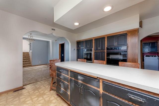 kitchen with dobule oven black, arched walkways, light countertops, washer / dryer, and light floors