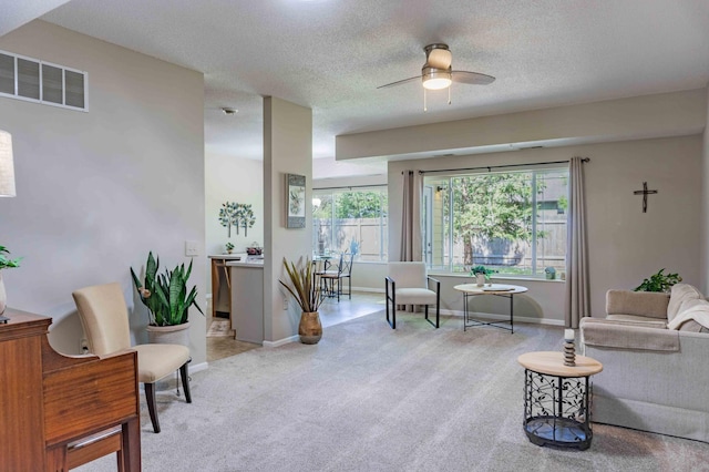 sitting room featuring a ceiling fan, light carpet, plenty of natural light, baseboards, and a textured ceiling