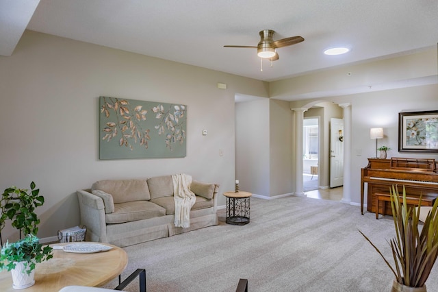 living area featuring decorative columns, arched walkways, ceiling fan, light colored carpet, and baseboards