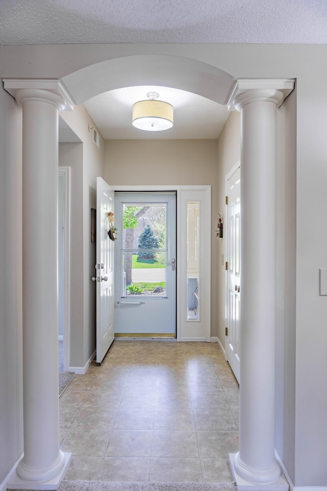 entrance foyer featuring ornate columns, arched walkways, light tile patterned floors, and baseboards