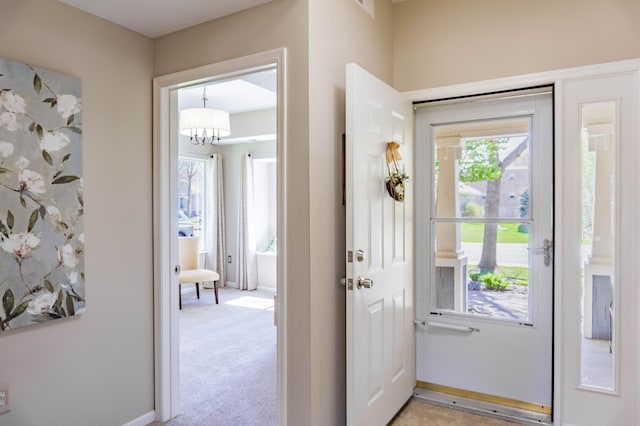 doorway with a chandelier, light carpet, and baseboards