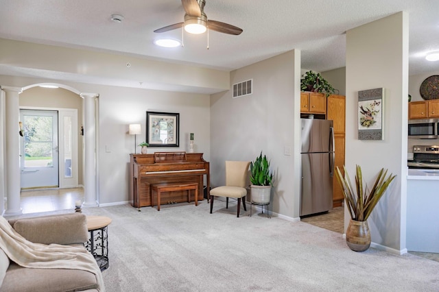 sitting room featuring decorative columns, light carpet, a ceiling fan, and arched walkways
