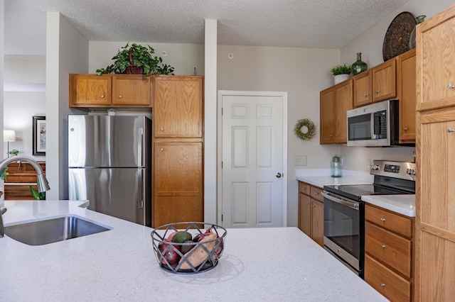 kitchen with stainless steel appliances, a sink, a textured ceiling, brown cabinets, and light stone counters