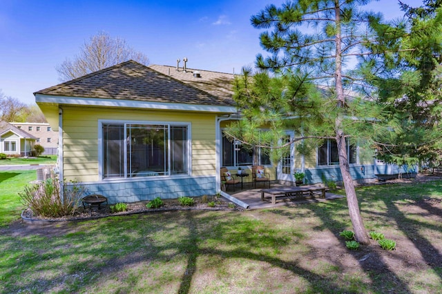 back of property with a shingled roof, a yard, and a patio area
