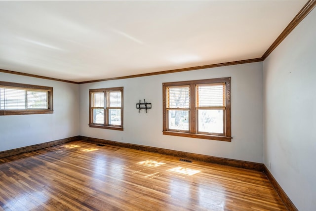 empty room with wood-type flooring, baseboards, and crown molding