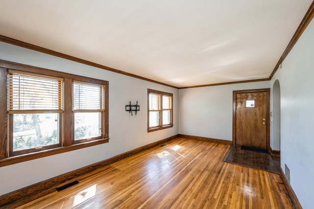 entrance foyer with arched walkways, light wood-type flooring, baseboards, and ornamental molding