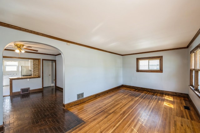 unfurnished living room featuring baseboards, arched walkways, a ceiling fan, healthy amount of natural light, and crown molding