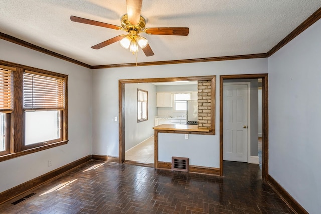 spare room with a textured ceiling, baseboards, ceiling fan, and crown molding