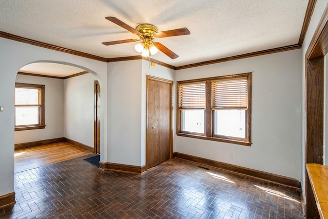 unfurnished room with arched walkways, baseboards, a ceiling fan, a textured ceiling, and ornamental molding