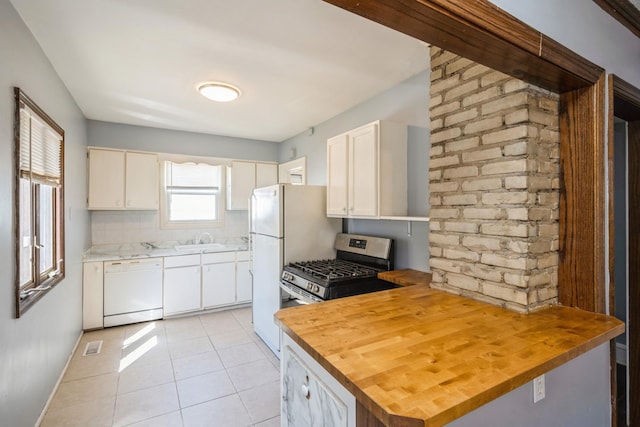 kitchen featuring dishwasher, stainless steel gas range, light tile patterned floors, a sink, and wood counters