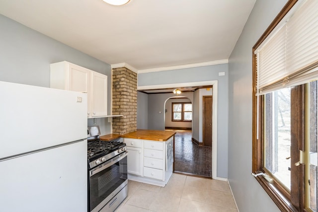 kitchen with freestanding refrigerator, gas stove, white cabinets, and arched walkways