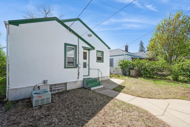 view of front of home featuring stucco siding, a front yard, and a cooling unit