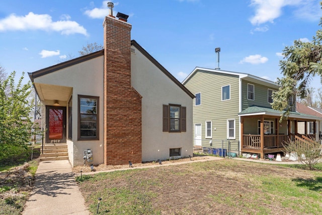 rear view of house featuring stucco siding and a chimney