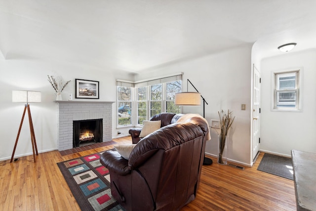 living area with a brick fireplace, baseboards, visible vents, and hardwood / wood-style floors