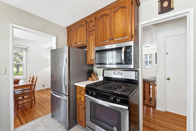 kitchen featuring brown cabinets, light countertops, baseboards, stainless steel appliances, and light wood-style flooring
