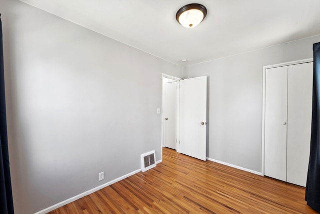 unfurnished bedroom with baseboards, visible vents, wood finished floors, and a closet