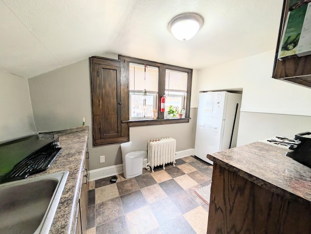 kitchen featuring dark brown cabinetry, a sink, radiator, freestanding refrigerator, and baseboards