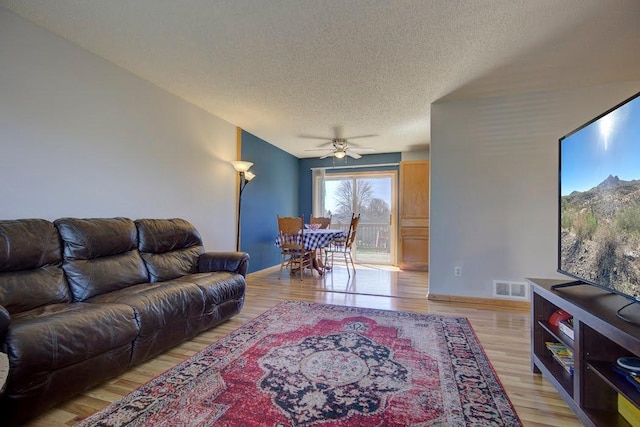 living area featuring a textured ceiling, a ceiling fan, baseboards, light wood-type flooring, and visible vents