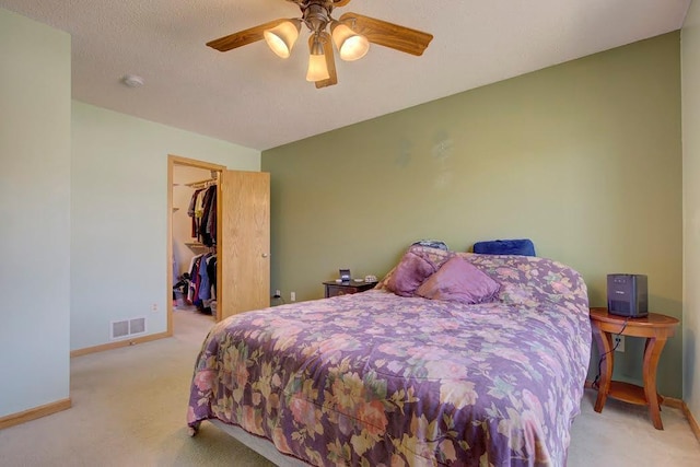 carpeted bedroom with a walk in closet, a ceiling fan, visible vents, baseboards, and a closet